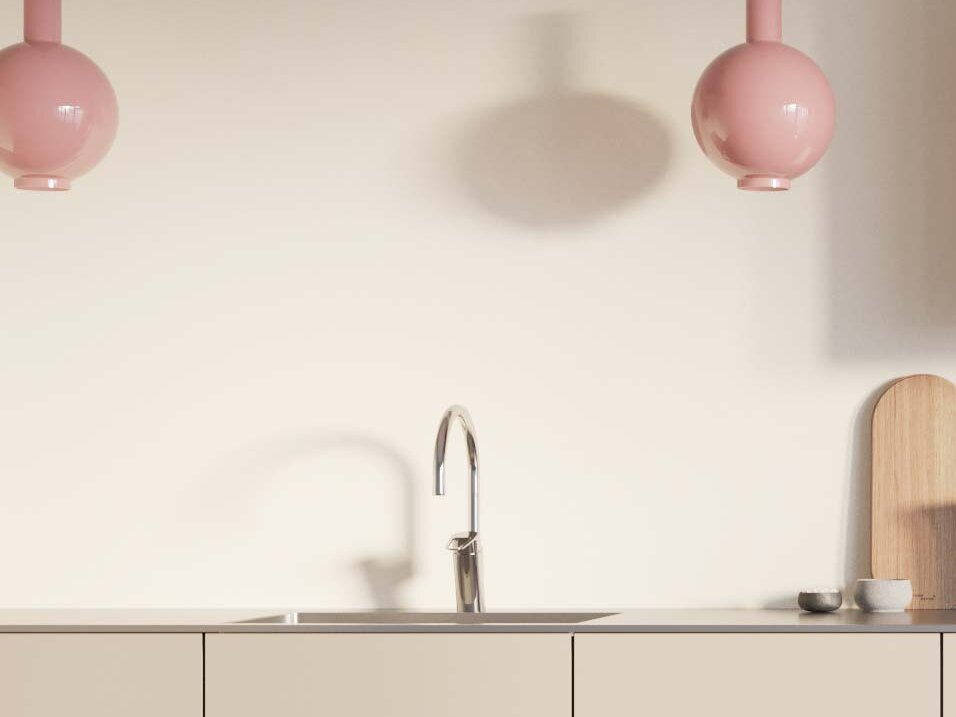 Minimalistiskt kök med ljusskåp, väggskåp i trä, två rosa taklampor och solljus som strömmar genom ett fönster.