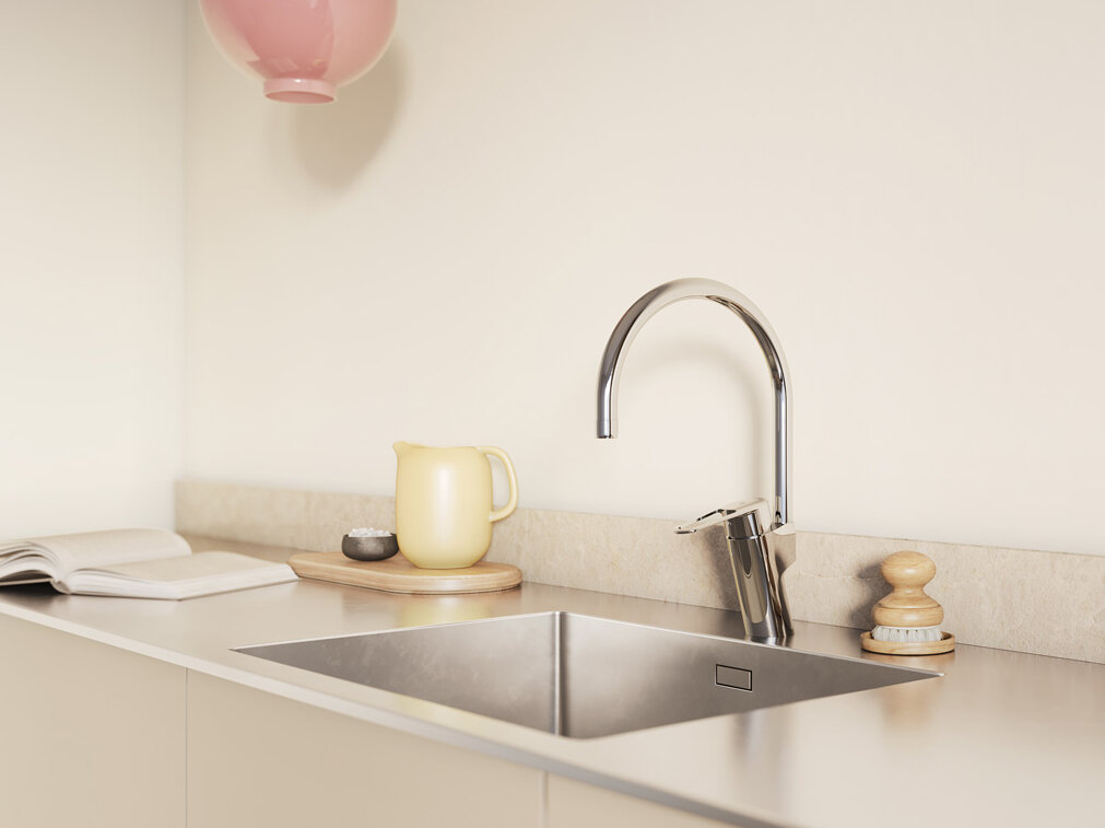 Minimalistiskt kök med ljusskåp, väggskåp i trä, två rosa taklampor och solljus som strömmar genom ett fönster.