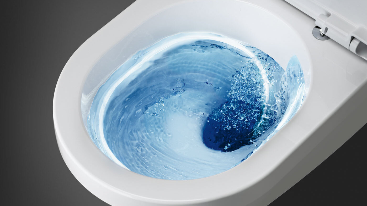 Et hvitt toalett med blått vann som virvler inni under spyling, sett ovenfra.