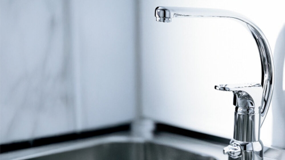 A chrome kitchen mixer sits above a stainless steel sink.