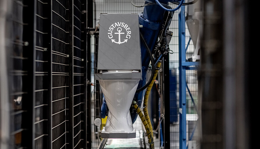 In a factory setting, a robotic arm handles a Gustavsberg toilet.