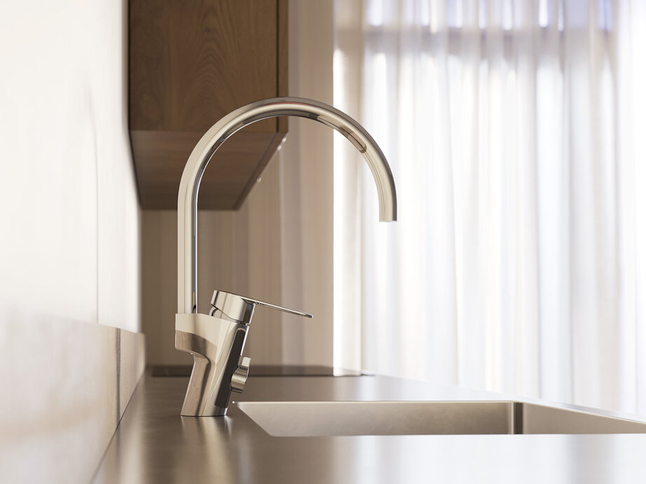 Close-up of a modern kitchen sink with a tall chrome kitchen mixer and natural light coming in through thin curtains in the background.