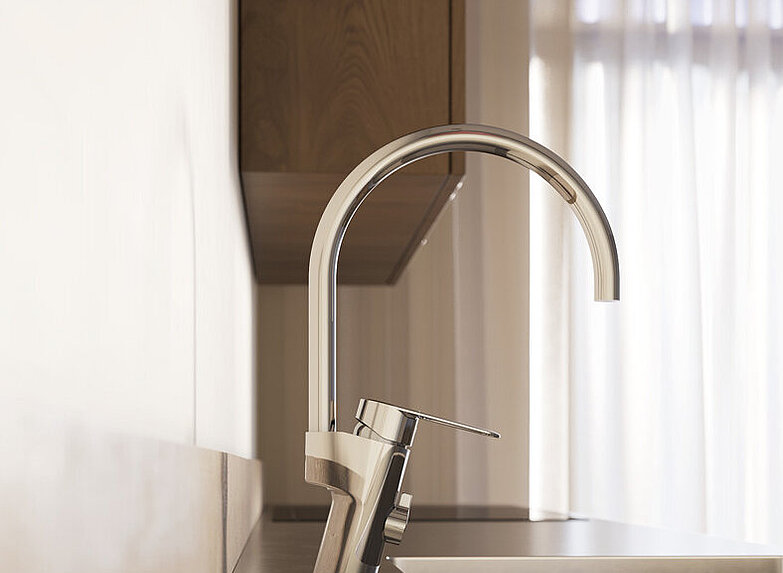 Lähivõte moodsast köögivalamust, millel on kõrge kroomitud köögisegisti ja taustal õhukeste kardinate kaudu paistev loomulik valgus.