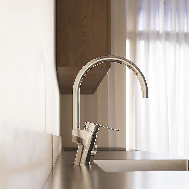 Close-up of a modern kitchen sink with a tall chrome kitchen mixer and natural light coming in through thin curtains in the background.