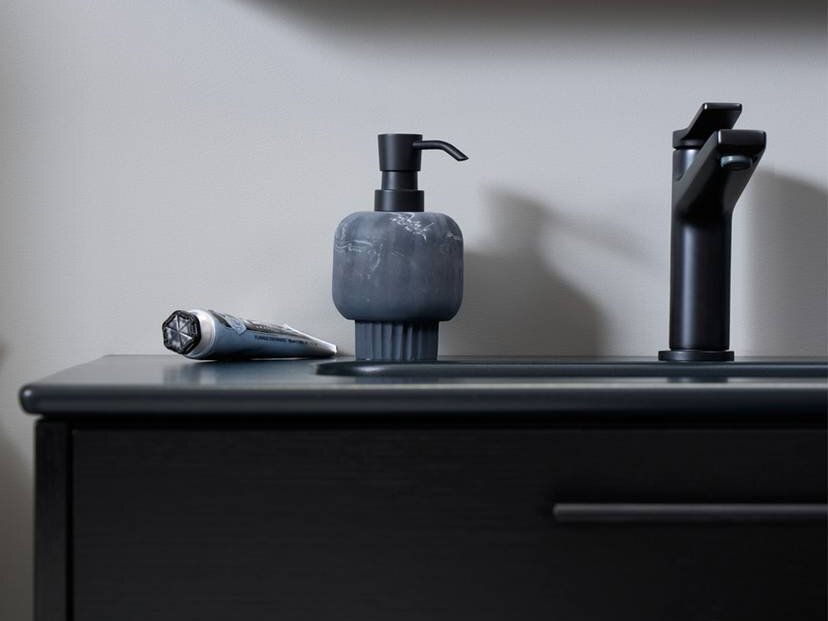Black bathroom counter with a soap dispenser, a toothpaste tube, and a black faucet in front of a mirror.