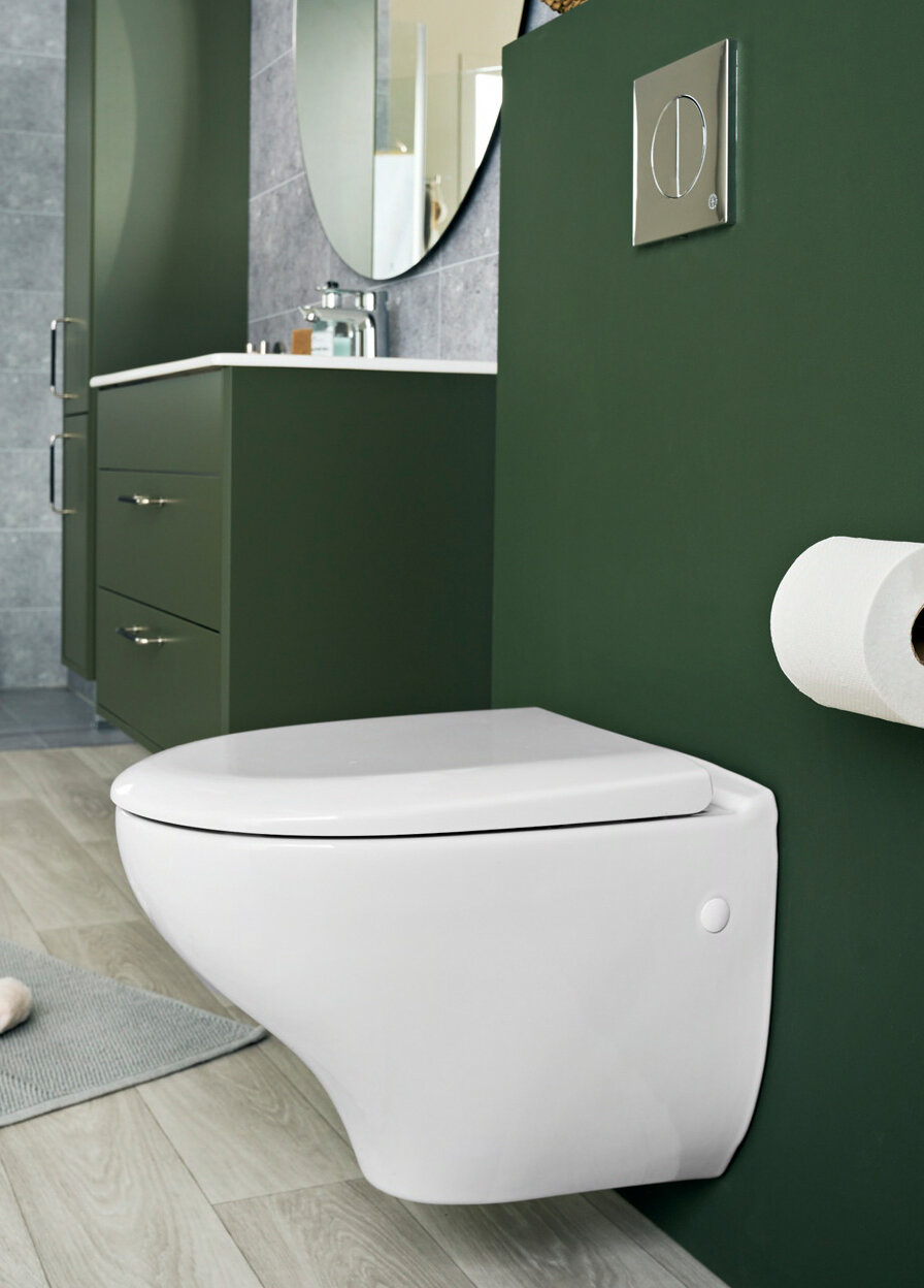 A wall-mounted toilet on a green wall. Green bathroom furniture and a large round mirror.