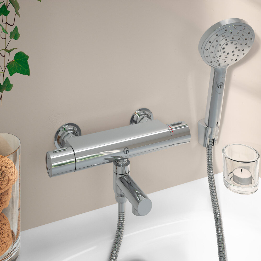 Wall-mounted chrome bathtub mixer and handheld showerhead with a candle and jar of bath items nearby.