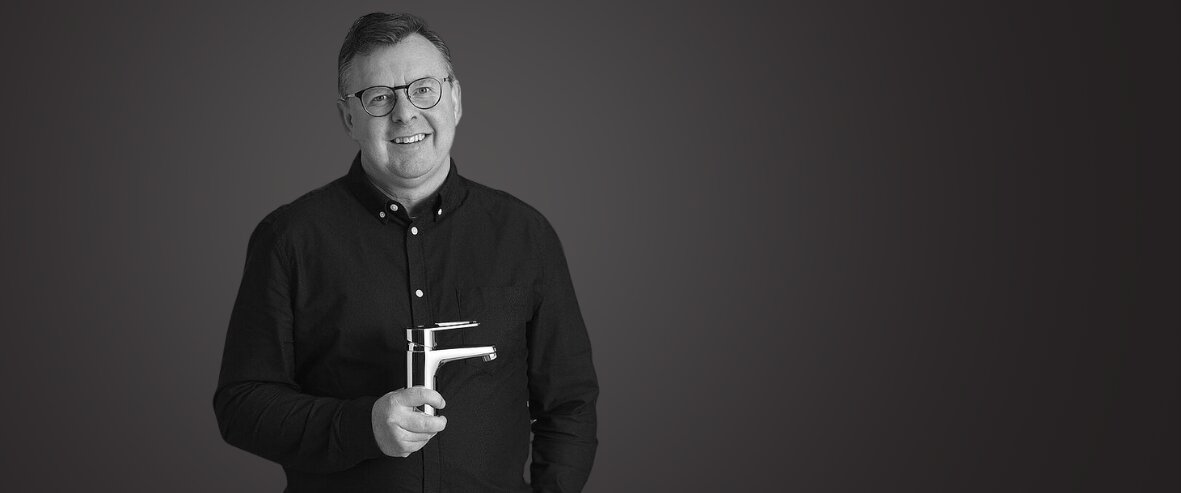 Mattias Virsgård i svart skjorte som holder en mikser, står mot en enkel mørk bakgrunn og smiler til kameraet.