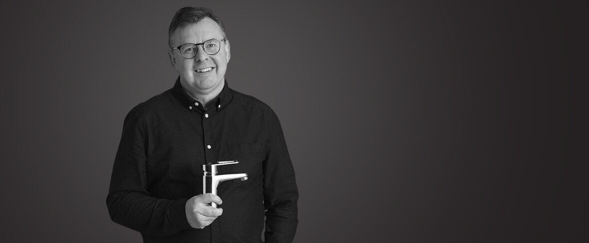Mattias Virsgård in a black shirt holding a mixer, standing against a plain dark background, smiling at the camera.