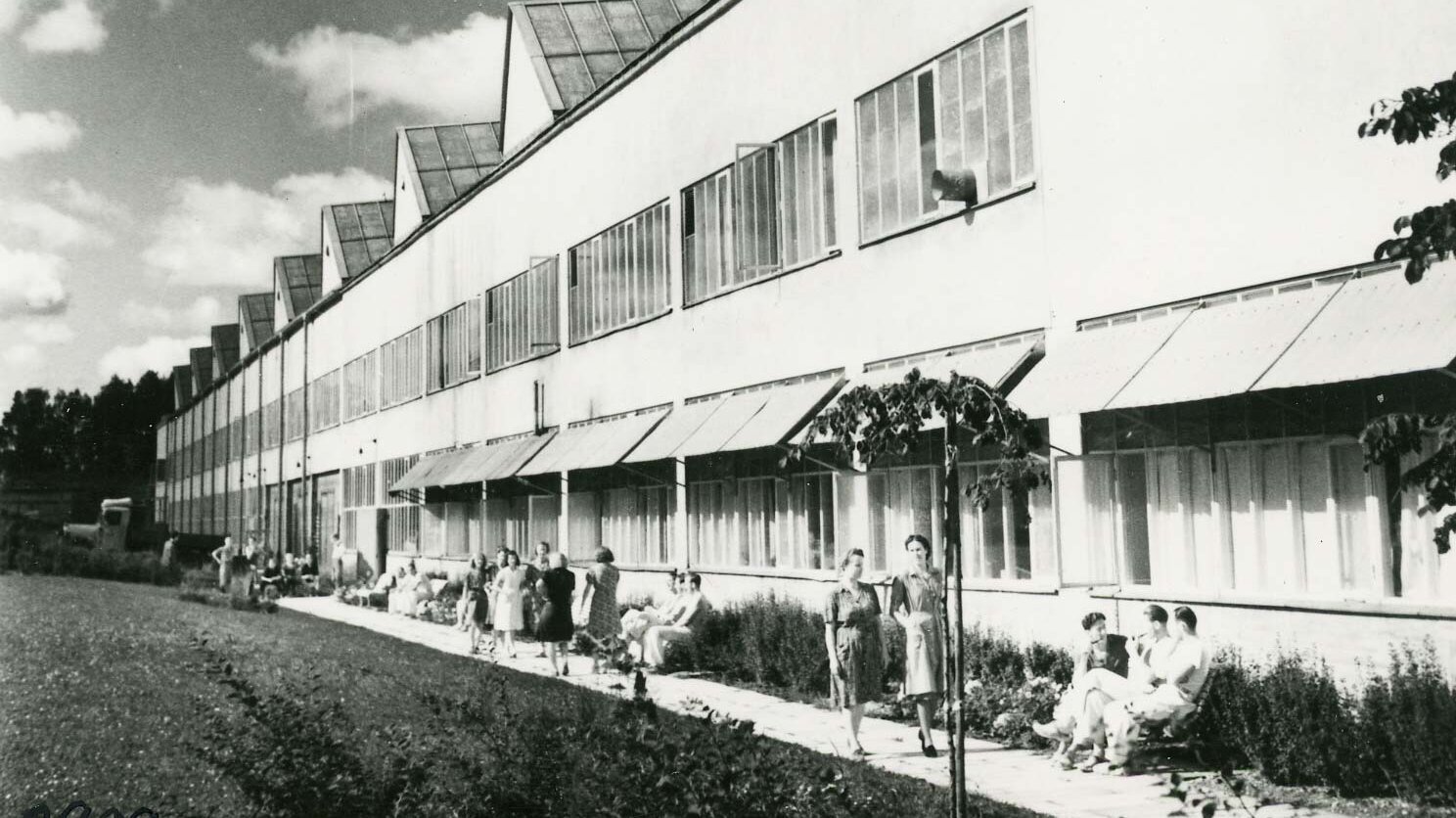 Nespalvotas Vårgårdos gamyklos, įsikūrusios prie upės su nedideliu tilteliu, medinių pastatų vaizdas.