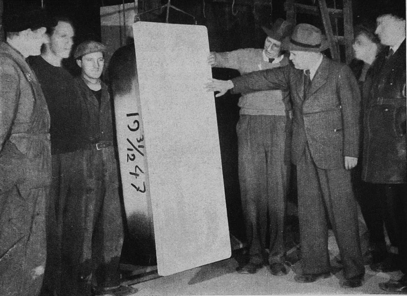 Grupė vyrų stovi aplinkui ir laiko „Gustavsberg“ vonią, ant kurios užrašyta data „1947-12-31“.