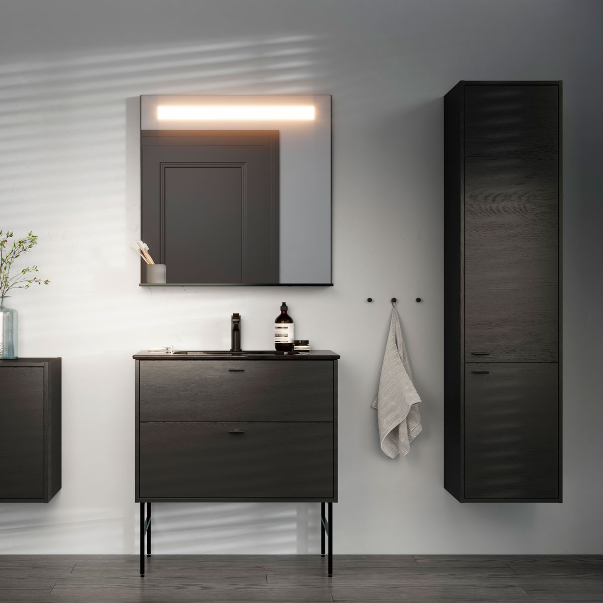 Bad med mørke treskap, et rektangulært speil med lys og et håndkle hengende på veggen.