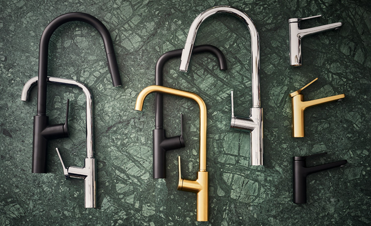 Kitchen and bathroom mixer in black, brass, and chrome on a green marble surface.