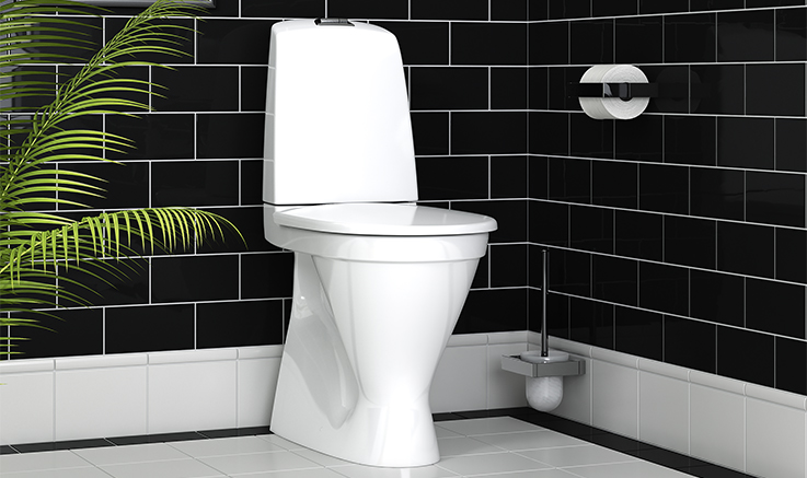 Golvstående vit toalett i hög modell från Gustavsberg installerad i ett modernt badrum med svart kakel, med en växt till vänster.